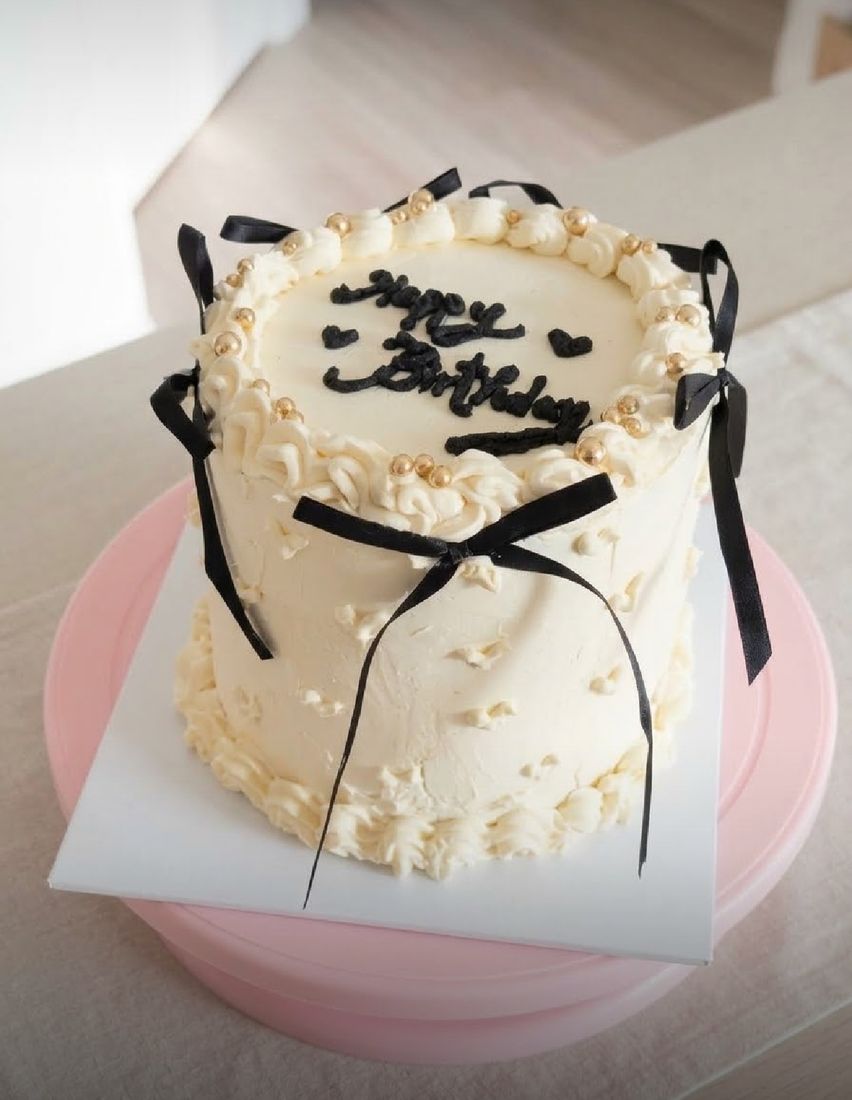 Pandan coconut cake with black ribbon bows, gold pearls and Happy Birthday piped on top
